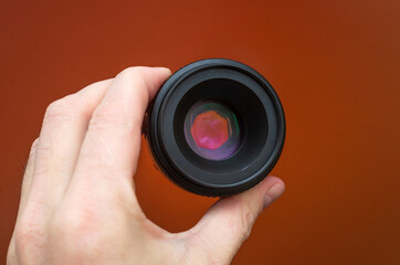male hand holding a camera lens on an orange background