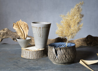 A vase, a glass and a handmade saucepan with pampas grass, a dried leaf stand on a wooden, sawn...