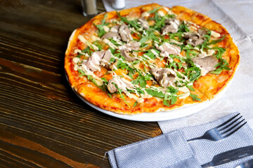 Meat mushroom pizza on a wooden table Nearby is a red bell pepper a salt shaker and a pepper shaker and cutlery.