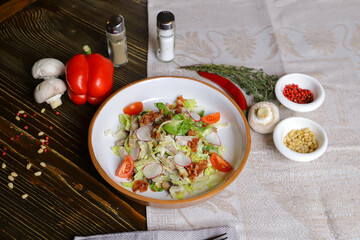 Salad with lettuce, cherry tomatoes, radish slices, herbs are served on a dark tabletop on a linen napkin. Hot red pepper and whole white champignon, rosemary branch.