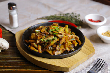 In a frying pan, fried potatoes are served on a wooden light stand, cutlery, hot red peppers, spices, white champignon.