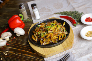 In a frying pan, fried potatoes are served on a wooden light stand, cutlery, hot red peppers, spices, white champignon.
