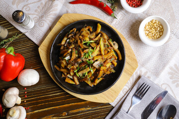 In a frying pan, fried potatoes are served on a wooden light stand, cutlery, hot red peppers, spices, white champignon.