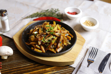 In a frying pan, fried potatoes are served on a wooden light stand, cutlery, hot red peppers, spices, white champignon.