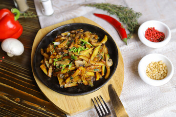 In a frying pan, fried potatoes are served on a wooden light stand, cutlery, hot red peppers, spices, white champignon.