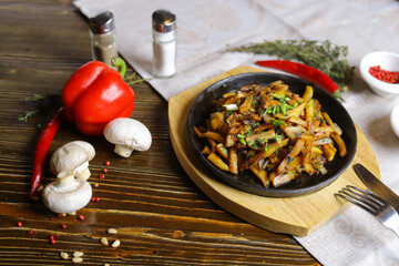 In a frying pan, fried potatoes are served on a wooden light stand, cutlery, hot red peppers, spices, white champignon.