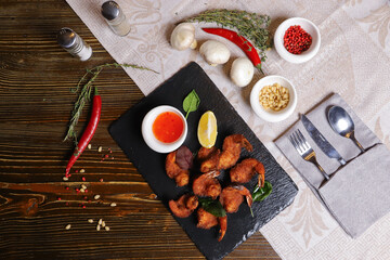 Shrimp is served with sauce. Tempura king prawns, sliced lemon, green basil leaves are served on a black stone stand. Cutlery, hot pepper pods, spices in bowls, white mushrooms.