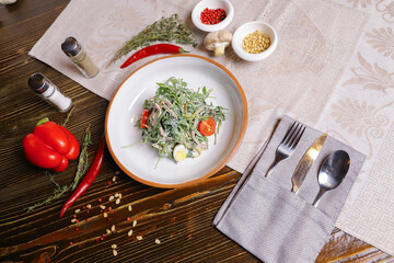 On a dark countertop, a light linen napkin, on a cutting board Served salad with rucola leaves, boiled tongue cut into long slices with sauce A couple of salt and pepper, cutlery, red peppers decorate