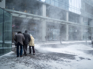 Natural disasters. People walk along the building through a blizzard with heavy snowfall. A snow...