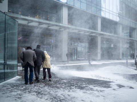 Natural Disasters. People Walk Along The Building Through A Blizzard With Heavy Snowfall. A Snow Cyclone Covered The City.