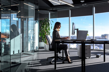Female boss working at computer in office, silhouette of business woman sitting at desk successful and independent director - obrazy, fototapety, plakaty