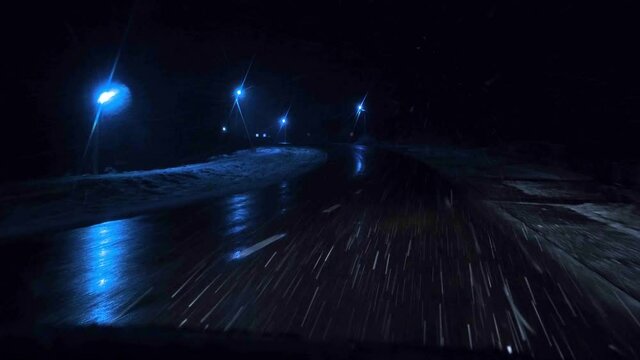 The first snow in winter at night, the view from the car while driving, the light of car headlights.