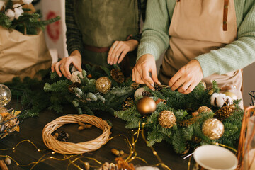 Two millennial women making Christmas wreath using pine branches and festive decorations. Small business