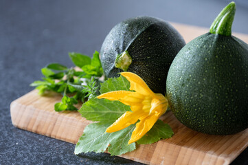 zwei Zucchini mit Blatt und Blüte auf Holzbrett und schwarzem Hintergrund