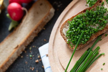 Schnittlauchbrot auf Holzbrett mit Brot und Radieschen im Hintergrund