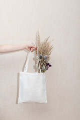 Mockup of a white tote reusable eco cotton shopper bag with dry grass and flowers on a white background. Eco friendly.