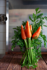 Bunch of fresh young carrots with green haulm  on wooden brown table in the kitchen.