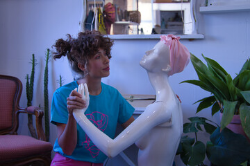 Young woman, designer, dressmaker and artist, with sad look holding hands with a female mannequin...