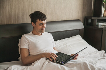 Man is sitting in bed in his bedroom and working on a laptop