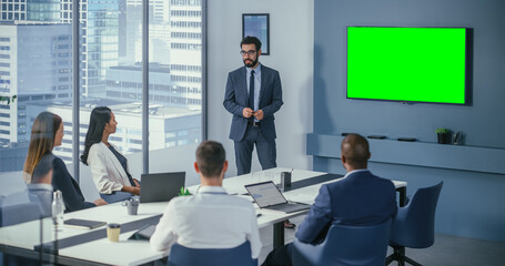 Diverse Office Conference Room Meeting: Male Project Manager Uses Green Screen Chroma Key Wall TV to Present Investment Opportunity for Investment Team. e-Commerce Product Strategy. Medium Wide