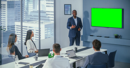 Diverse Office Conference Room Meeting: Successful Black Male Project Manager Uses Green Screen Chroma Key Wall TV Presenting Product to Group of Investors. e-Commerce Strategy. Wide Static Shot