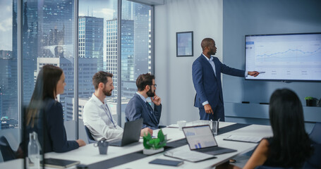 Diverse Office Conference Room Meeting: Charismatic Black Digital Entrepreneur Presents e-Commerce Fintech Product to a Group of Investors. Wall TV with Big Data Analysis, Infographics, Statistics