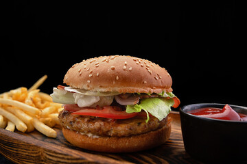 Burger with meat tomatoes and cheese, french fries and sauce, on a black background