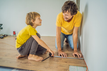 Father and son installing new wooden laminate flooring on a warm film floor. Infrared floor heating...
