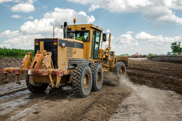 The grader performs excavation work on the construction of the road. - obrazy, fototapety, plakaty