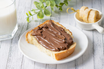 a sandwich with chocolate paste, milk and banana slices on a white wooden background. Green branch. Delicious breakfast