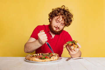 Portrait of red- bearded man getting ready to eat delicious Italian pizza isolated on yellow studio background.