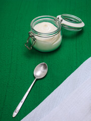 homemade mayonnaise in glass jar and spoon on green background