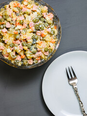 crystal salad bowl with olivier and white plate with fork on gray background close up