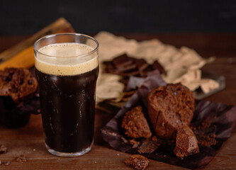 Glass of beer stout standing on wooden board next to chocolate muffin