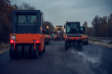 Asphalt rollers rolling new hot asphalt at dusk. Road construction.