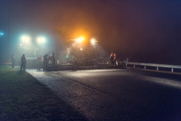 Laying asphalt paver at night with headlights. Road construction.