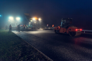 Laying asphalt paver at night with headlights. Road construction.