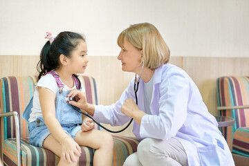 Smiling Doctor checking girl patient with stethoscope in hospital