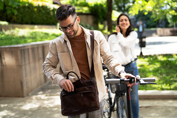 Fototapeta na wymiar Happy young couple outdoors. Loving couple with bicycle in the park, Handsome man using the phone.