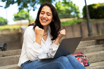 Young businesswoman sitting on steps outdoors and working on laptop. Beautiful girl learning in the park..