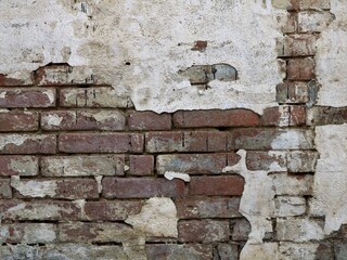 old dilapidated brick wall with layers of plaster as an antique exterior background, destroyed masonry of a building with fallen off mortar stucco,grunge urban backdrop with shabby texture 