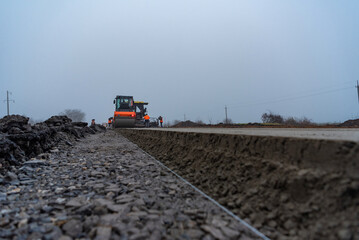 A roller compacts a layer of fresh concrete after a paver on a new road construction.
