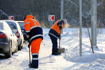 Snow removal in winter city at frost weather. Two men workers in uniform with a shovel and crowbar...
