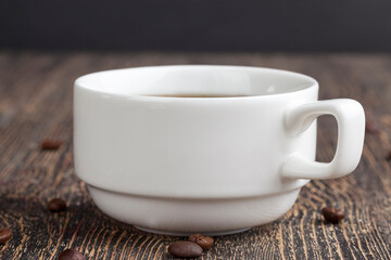 a white mug with a black drink and coffee beans