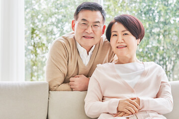 Middle-aged couple smiling while leaning on the sofa in the living room at home and looking at the...