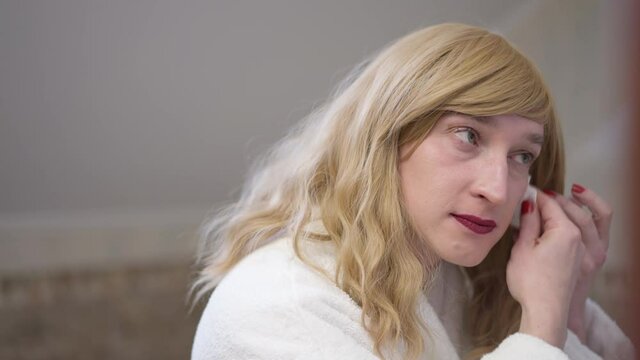 Side view close-up transgender woman removing makeup in bathroom. Confident Caucasian LGBT gender-fluid person using cotton pad rubbing face. Cosmetics and individuality