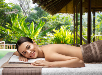 wellness, beauty and relaxation concept - young woman lying at spa or massage parlor over bungalow at exotic resort in thailand on background
