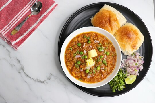  Indian Mumbai Street style Pav Bhaji, garnished with peas, raw onions, coriander, and Butter. Spicy thick curry made of out mixed vegetables served with pav over white background with copy space.