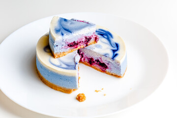 Piece of blue and white cheesecake with blueberry, cherry and black currant sauce inside on white plate on white table
