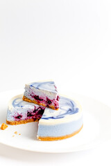Piece of blue and white cheesecake with blueberry, cherry and black currant sauce inside on white plate on white table